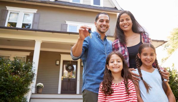 Husband and wife next to their 2 daughters holding keys to their home